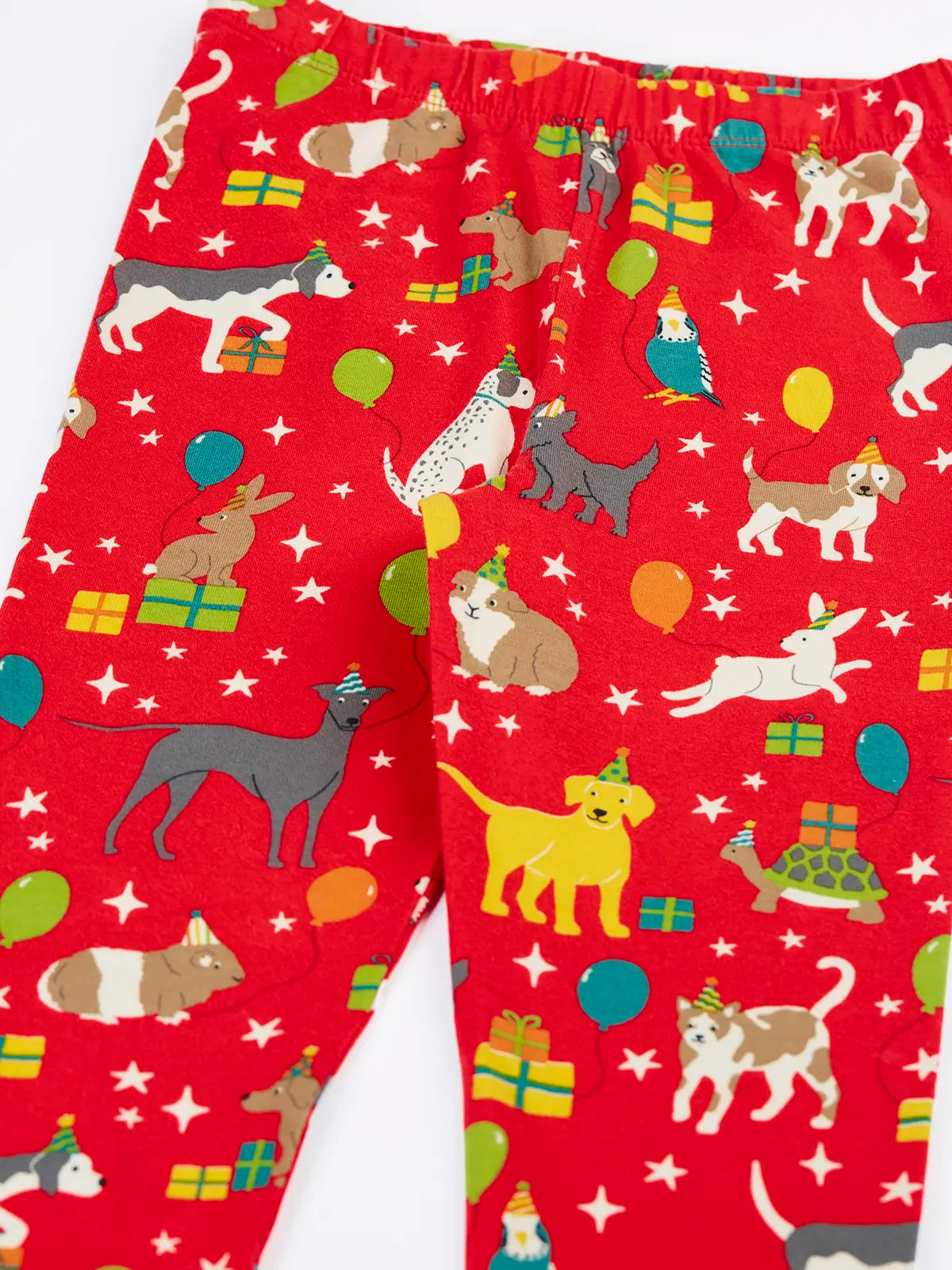 Close up of the Frugi organic cotton libby leggings with a perfect paw-ty party print showing the elasticated waist. Red background with all over print featuring pets with party hats surrounded by gifts and baloons.