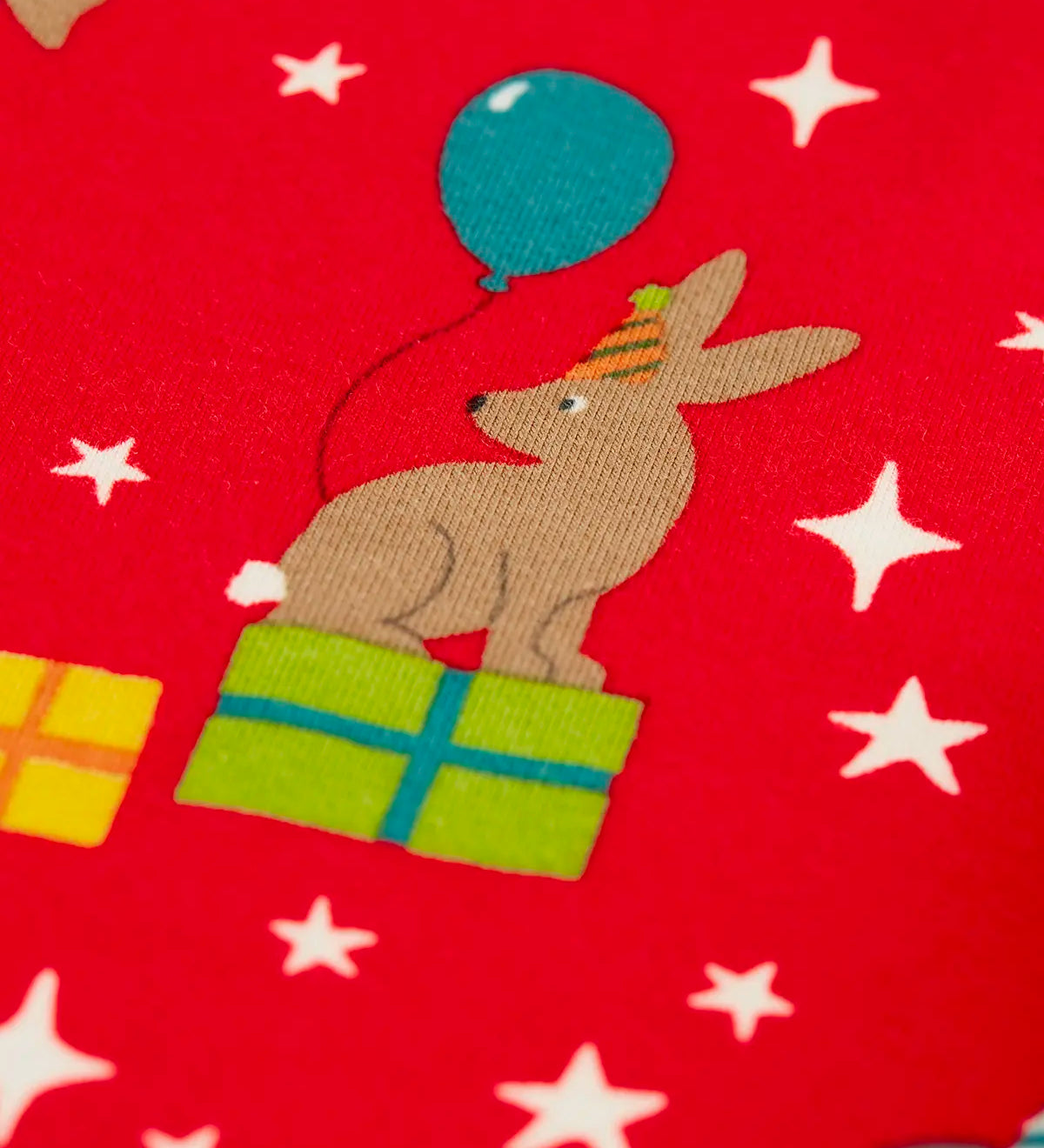 Close up of the rabbit on the Frugi organic cotton libby leggings with a perfect paw-ty party print. Red background with all over print featuring pets with party hats surrounded by gifts and baloons.