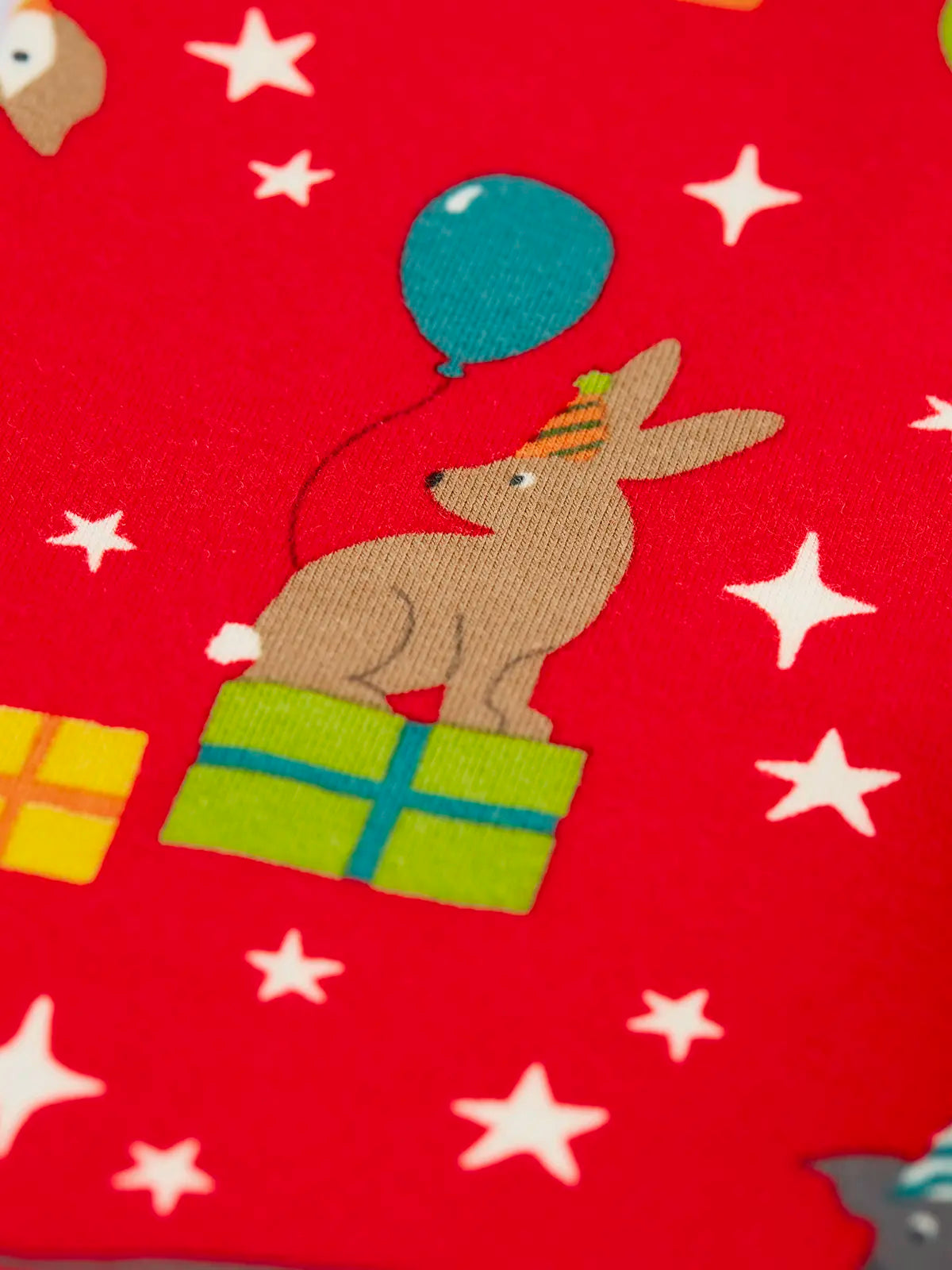 Close up of the rabbit on the Frugi organic cotton libby leggings with a perfect paw-ty party print. Red background with all over print featuring pets with party hats surrounded by gifts and baloons.