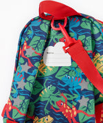 A close up of the Frugi little adventures be hoppy backpack showing the name tag on the back of the bag and the handy red rein attached by a clip