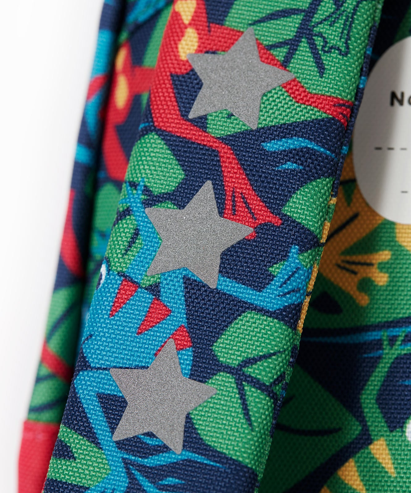 A close up of the shoulder strap of the Frugi little adventures be hoppy backpack showing the reflective stars and frog print detail