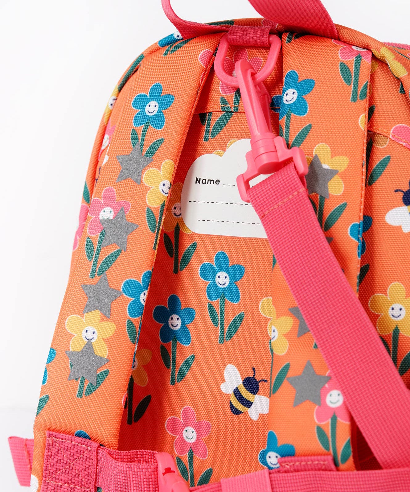 A close up of the Frugi little adventures fun flowers backpack showing the name tag on the back of the bag and the handy pink rein clip detail