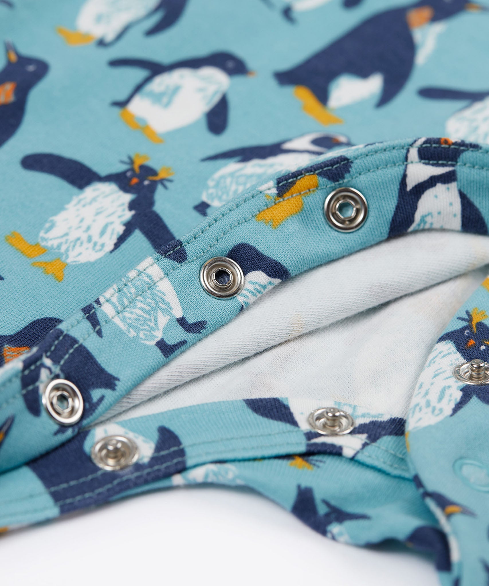 A close up of the popper closure on the Frugi Lovely babygrow in a blue penguin waddle design.