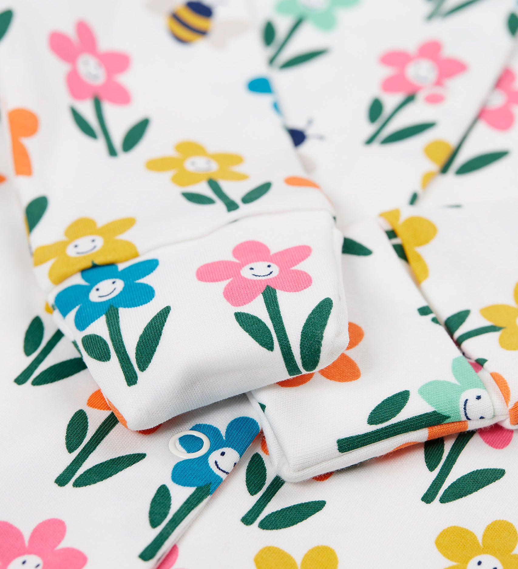 A close up of the fold-able sleeves on the Frugi Lovely Babygrow with a white fun flowers design. The fold-able cuffs can be folded over to use as scratch mitts.  