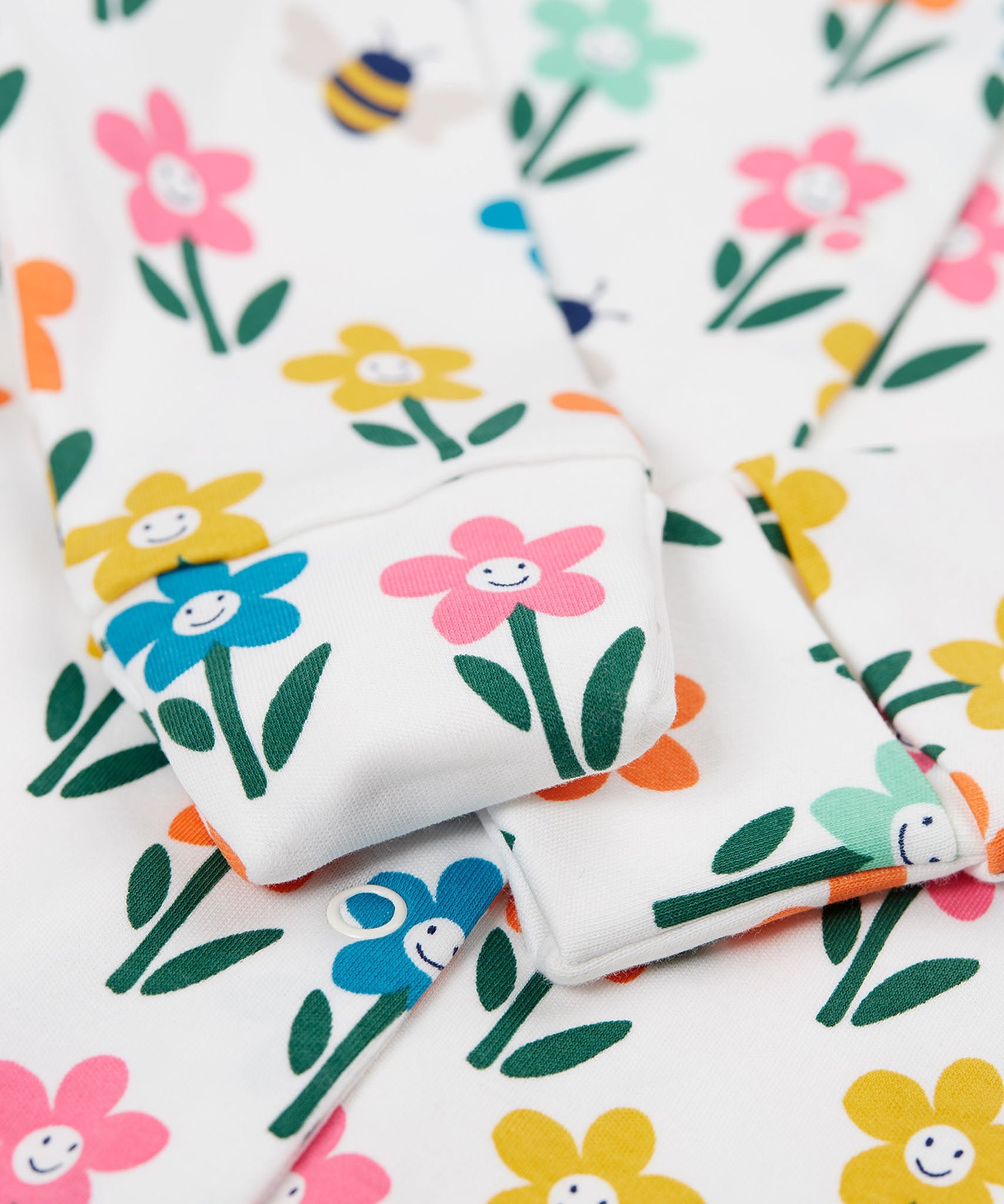 A close up of the fold-able sleeves on the Frugi Lovely Babygrow with a white fun flowers design. The fold-able cuffs can be folded over to use as scratch mitts.  