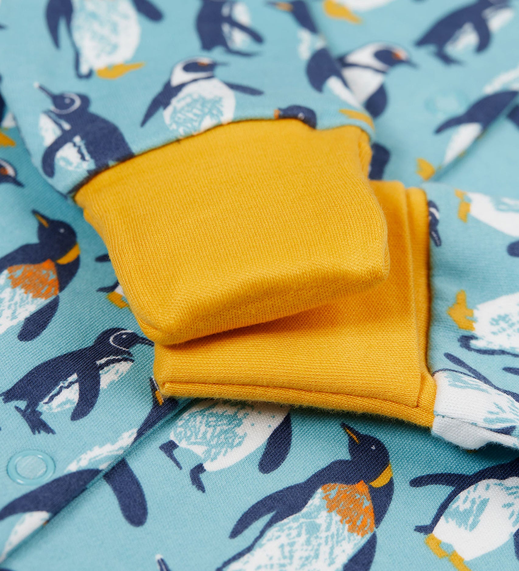 A close of the yellow gold coloured fold-able cuffs on the Frugi Lovely babygrow in a blue penguin waddle design.