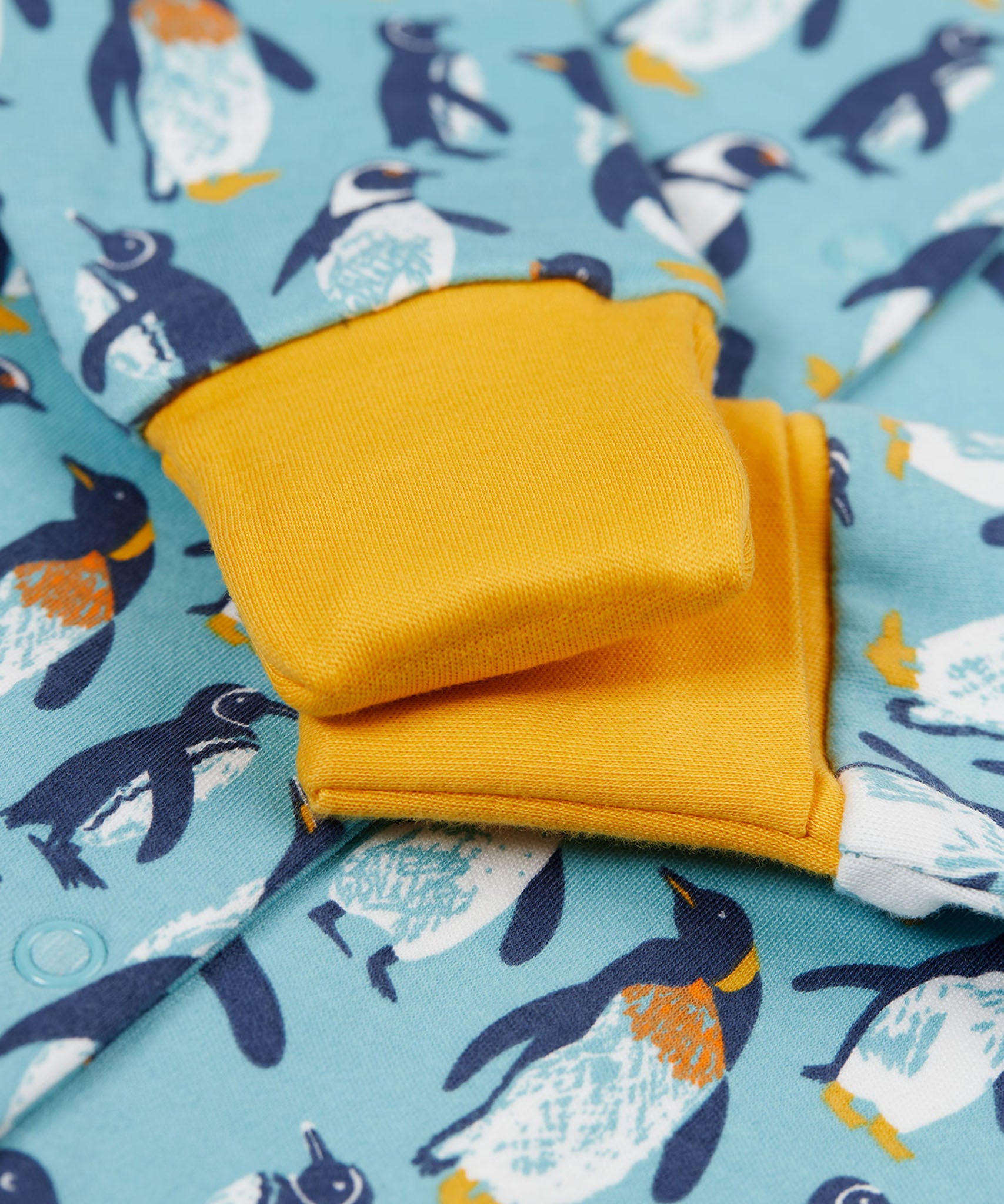 A close of the yellow gold coloured fold-able cuffs on the Frugi Lovely babygrow in a blue penguin waddle design.