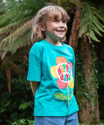 A child wearing the Frugi  Happy Days Mabe Relaxed T-Shirt. A turquoise blue organic cotton t-shirt with a large flower applique design on the front.The words Happy Days are placed on the centre of the flower applique. 