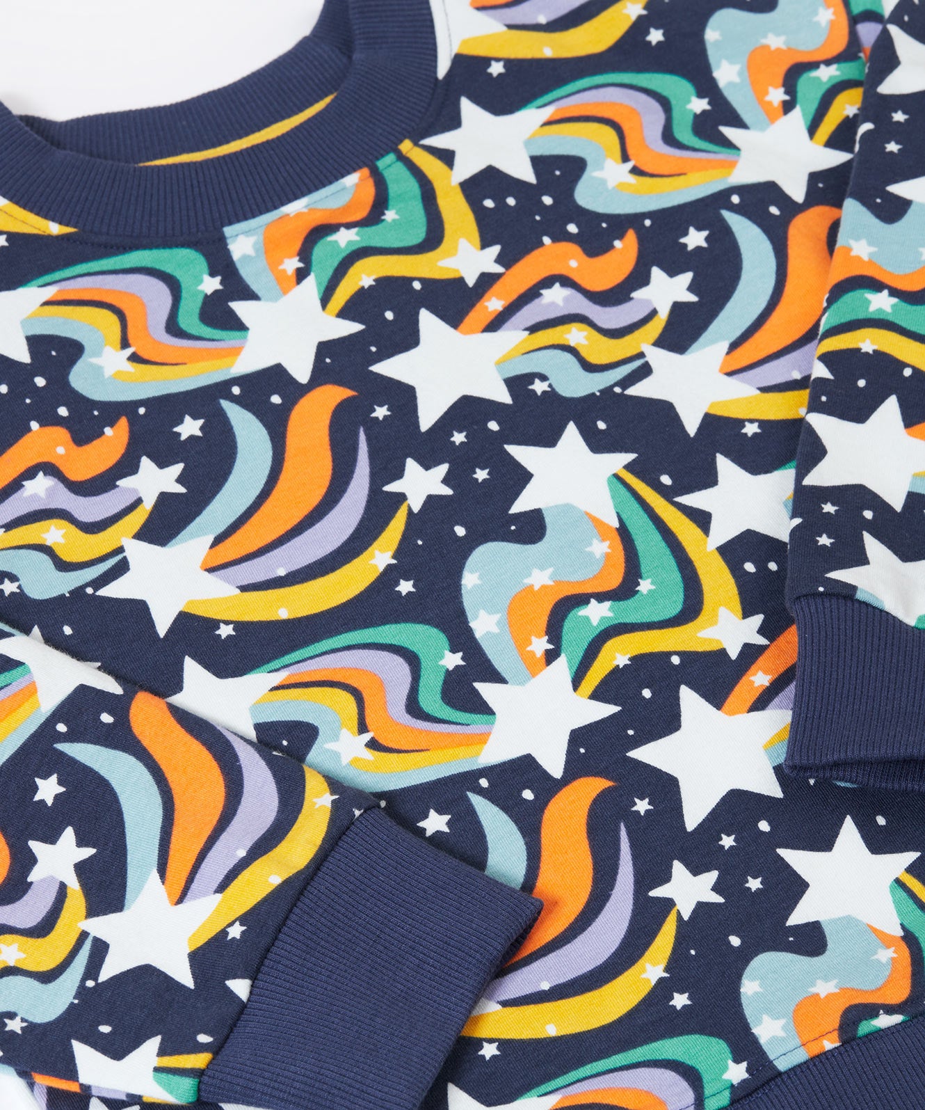 A close up of the print on the Frugi child's Organic Cotton Mawnan Jumper with a Magic Skies print. A navy background with white stars and rainbow swirls all over. This jumper is a part of a wide range of organic cotton clothing for children available here at Babipur. 
