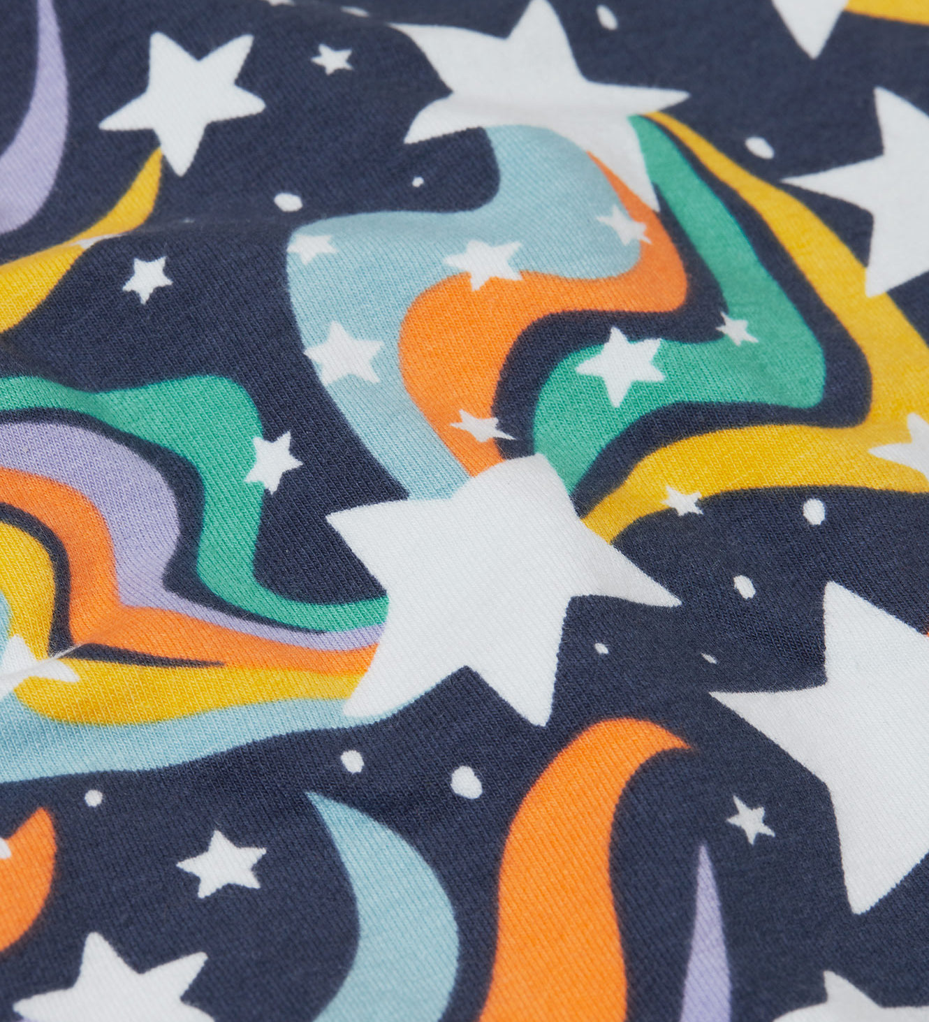 A close up of the print on the Frugi child's Organic Cotton Mawnan Jumper with a Magic Skies print. A navy background with white stars and rainbow swirls all over. This jumper is a part of a wide range of organic cotton clothing for children available here at Babipur. 