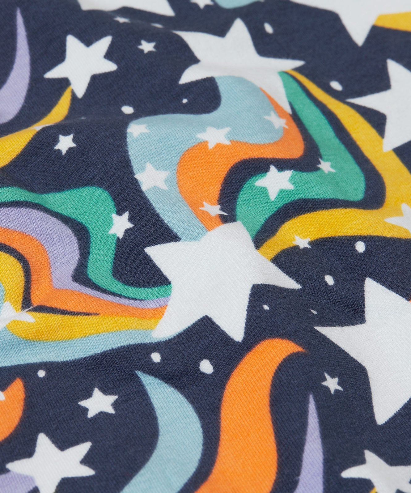 A close up of the print on the Frugi child's Organic Cotton Mawnan Jumper with a Magic Skies print. A navy background with white stars and rainbow swirls all over. This jumper is a part of a wide range of organic cotton clothing for children available here at Babipur. 