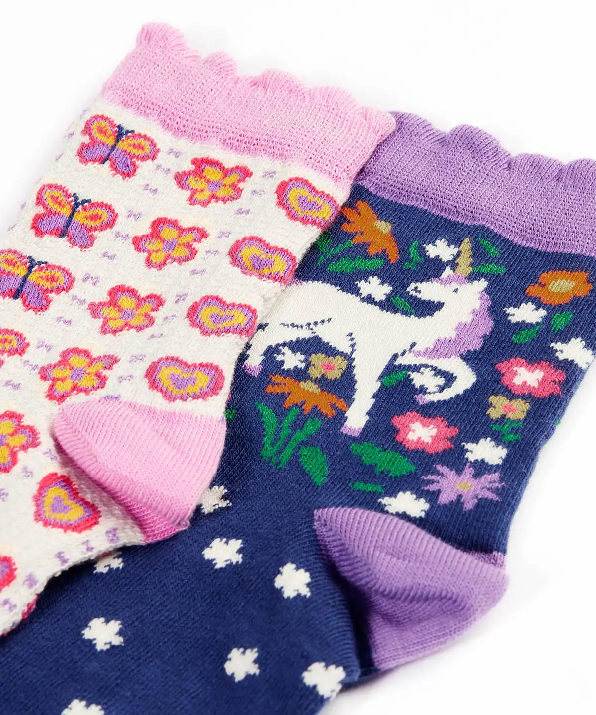 Close up of the Frugi magical organic cotton frill socks 2 pack. One navy pair with flowers and a pegasus and a purple frill. One white pair with flowers and butterflies with pink frill.