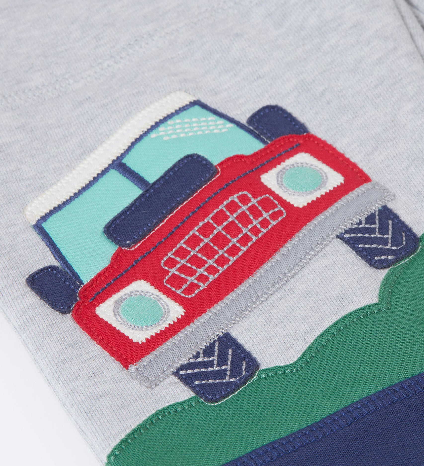 A close up of the red truck applique on the Frugi Malpas Placement Grey Joggers with Trucks.