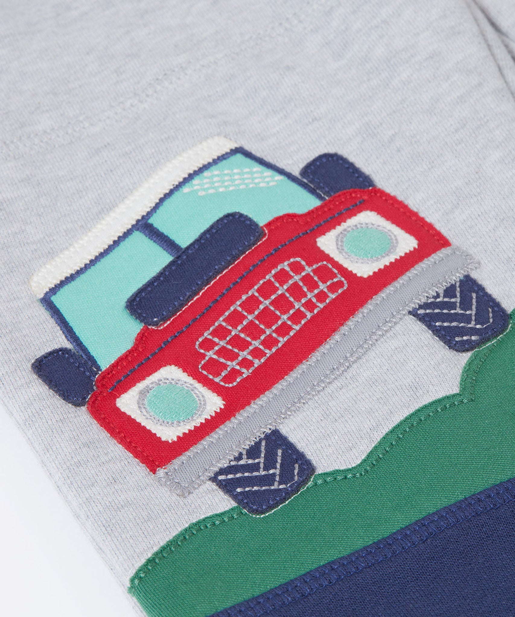 A close up of the red truck applique on the Frugi Malpas Placement Grey Joggers with Trucks.