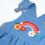 Close up of the rainbow details and button up straps on the Frugi mia denim dungaree with ruffle shoulders and rainbow applique design on the front.