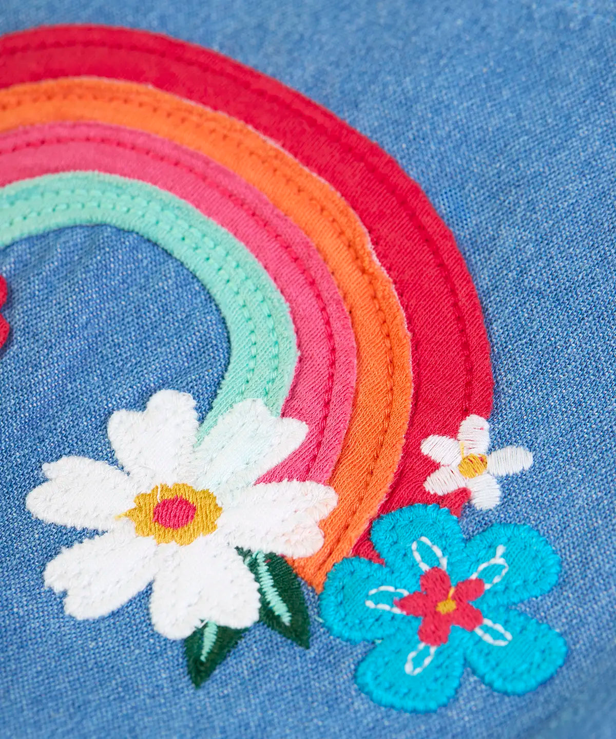 Close up of the rainbow and flower applique on the front of the Frugi mia organic cotton denim dungaree.