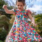 A toddler wearing Frugi Morwenna Skater Dress in the Birds Of Paradise print. Featuring different exotic birds surrounded by colourful flowers and leaves, twirling around amongst palm trees.