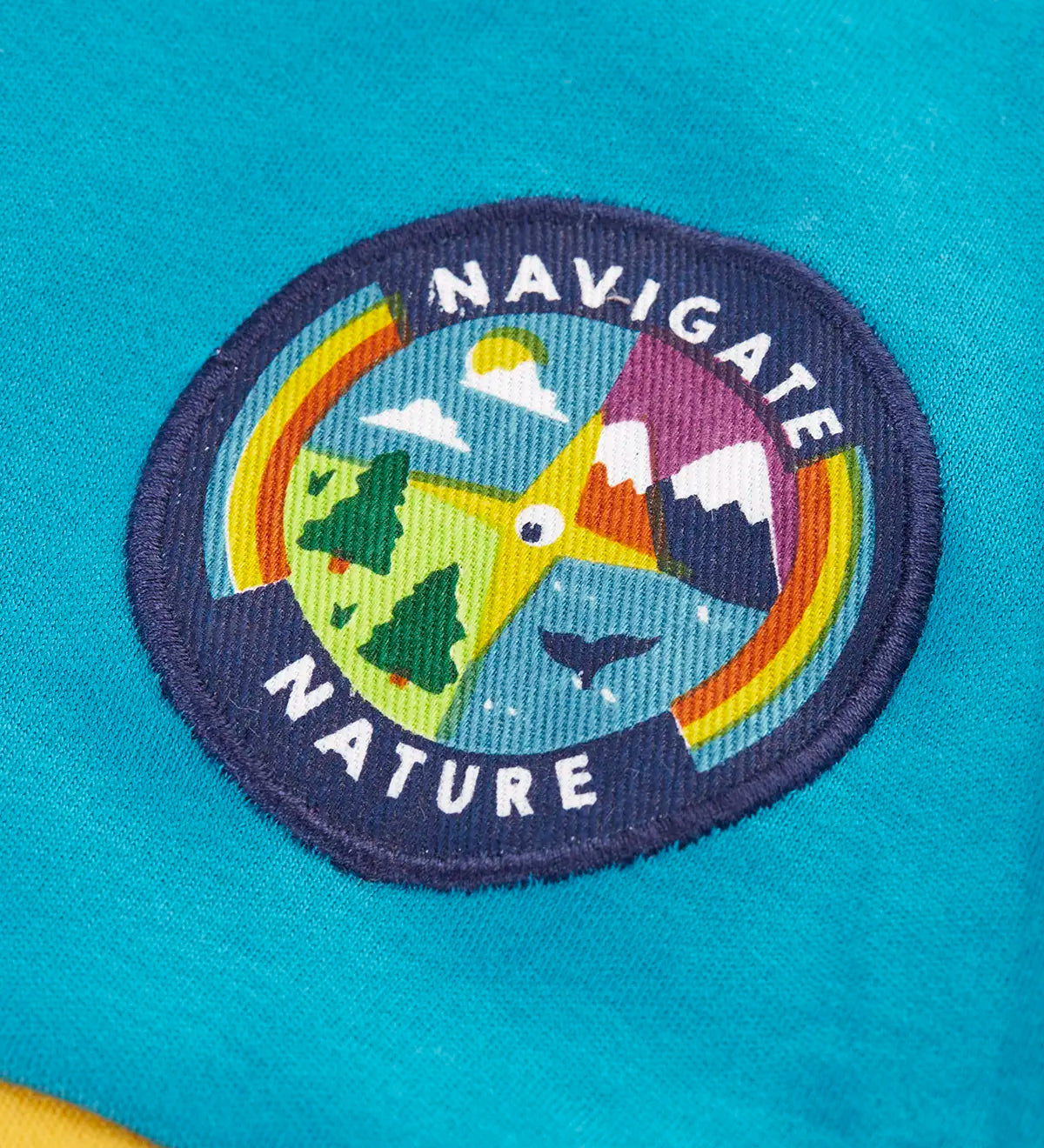 Close up of the navigate nature circular badge on the chest of the Frugi mullion long sleeve organic cotton rugby top.
