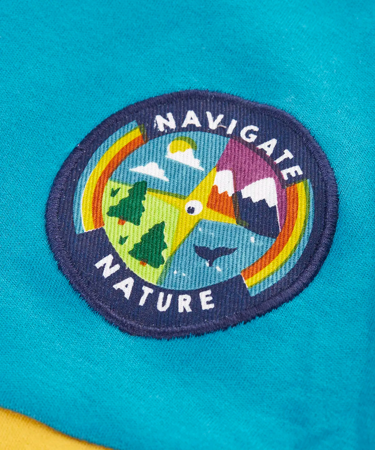 Close up of the navigate nature circular badge on the chest of the Frugi mullion long sleeve organic cotton rugby top.