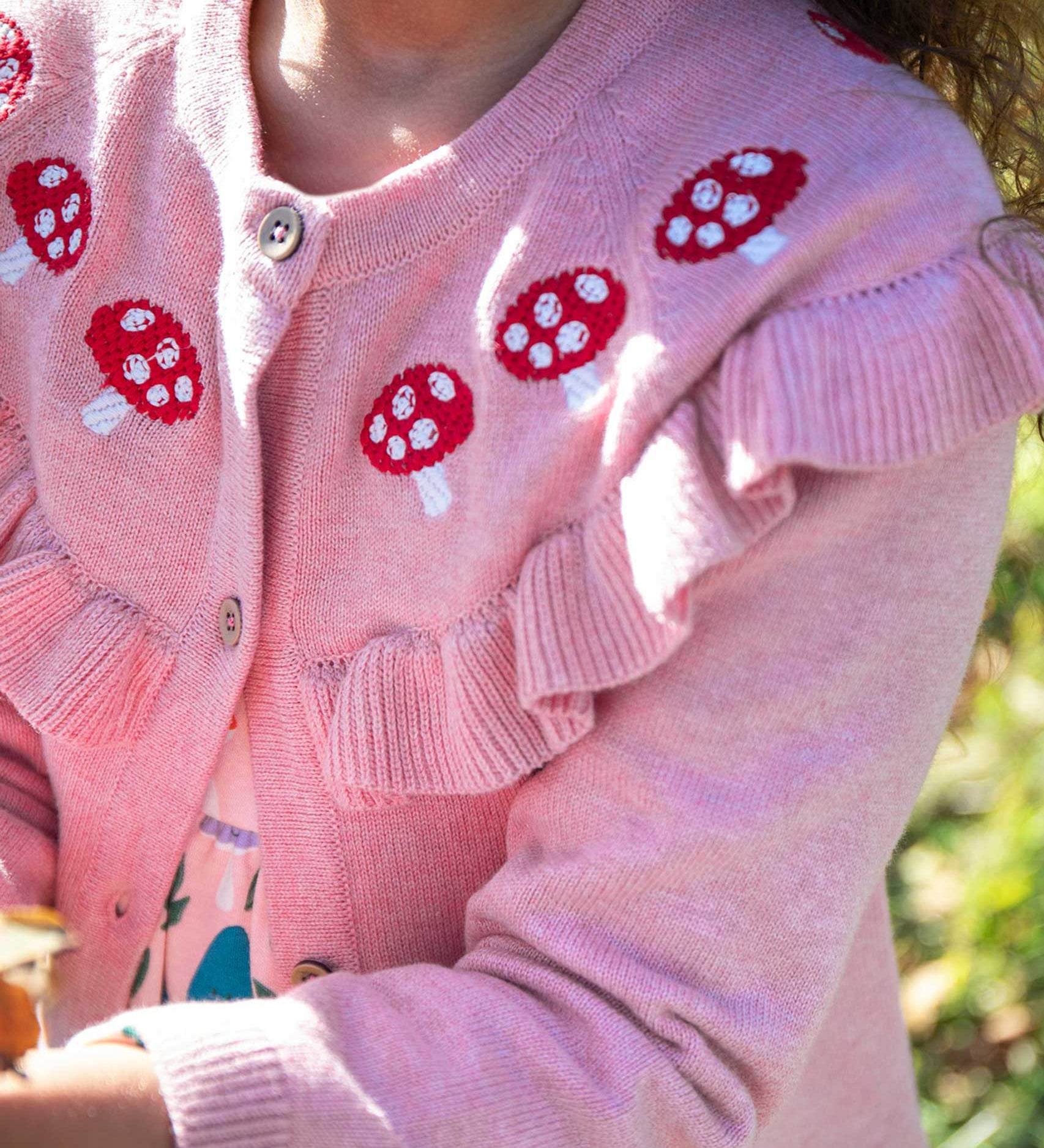 A close up of the mushrrom details on the Frugi pink marl Romi cardigan. A child is wearing the organic cotton cardigan.
