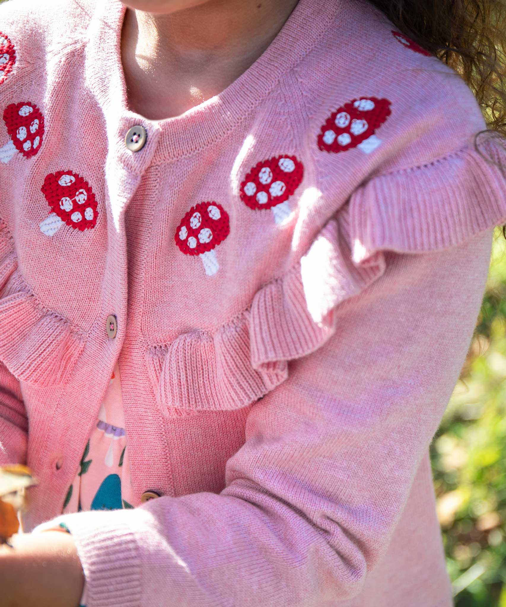 A close up of the mushrrom details on the Frugi pink marl Romi cardigan. A child is wearing the organic cotton cardigan.