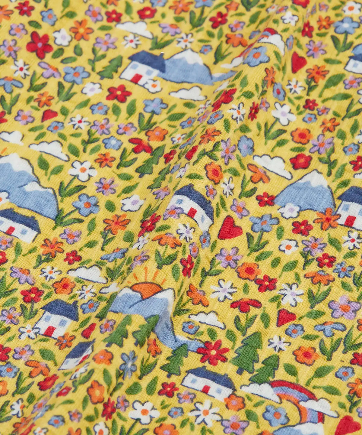 Close up of the highland houses themed print on the Frugi Natasha long sleeve organic cotton top in yellow. The print features flowers, mountains and a simple white house.