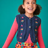 Child wearing the Frugi organic cotton connie navy knitted waistcoat with embroidered flower details, wooden button closure and scalloped edges with a pink long sleeve top underneath