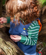 A close up of a toddler wearing the A toddler standing outside wearing the Frugi navy waterproof dungarees showing the yellow popper and orange fleece detail