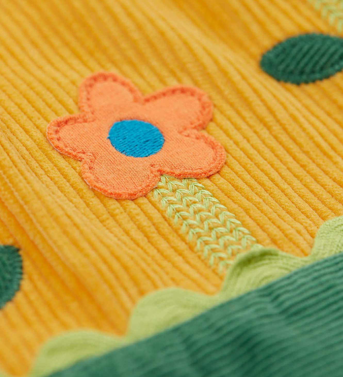 A close up of the flower applique detailing on the skirt of the Frugi Nellie Organic Cotton yellow gold Corduroy Pinafore Dress with Flowers. This dress is a part of a wide range of organic cotton clothing for children available here at Babipur. 
