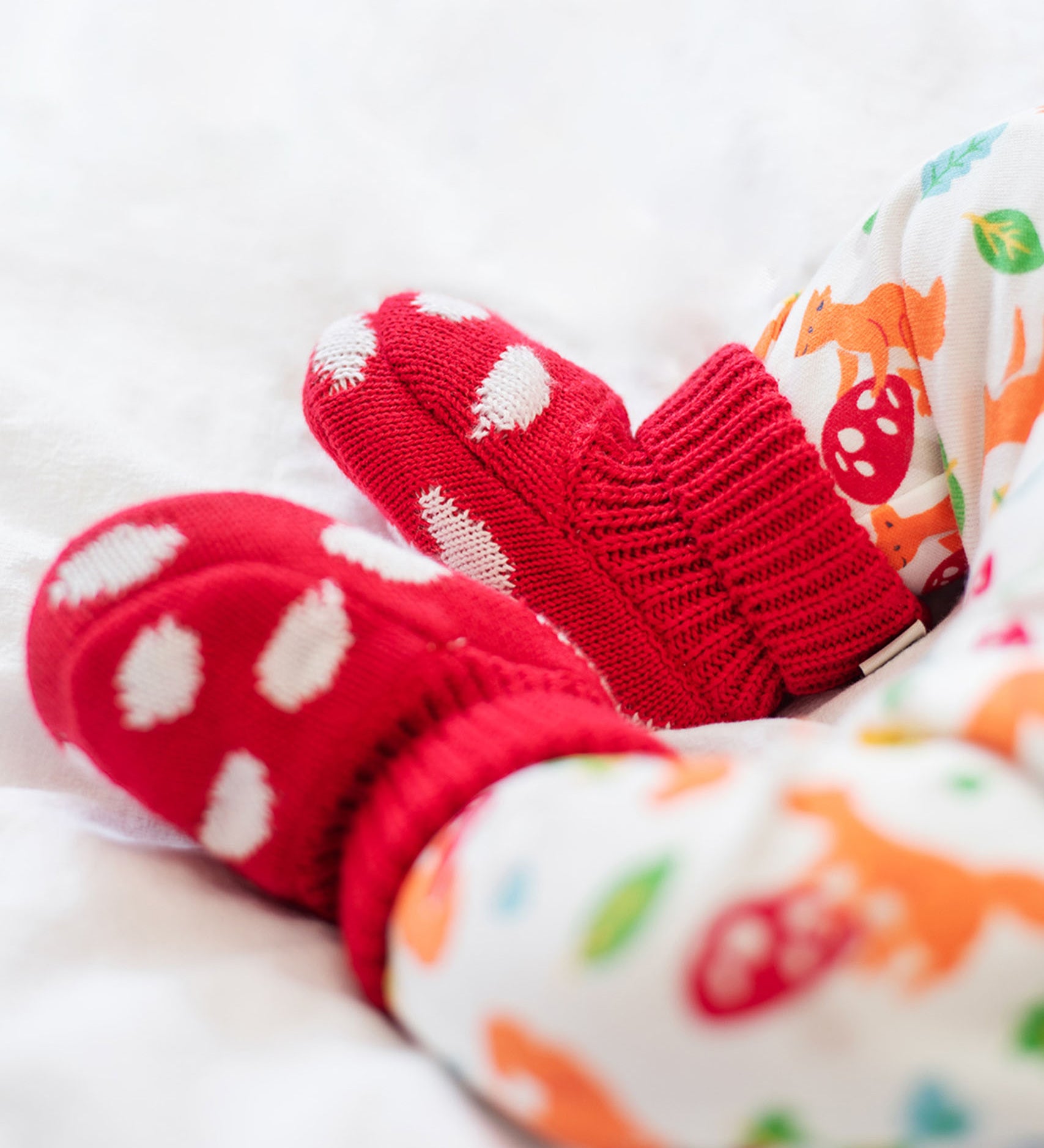 A close up of a baby wearing the Frugi kids noa knitted booties in red mushroom showing the knit detail. 