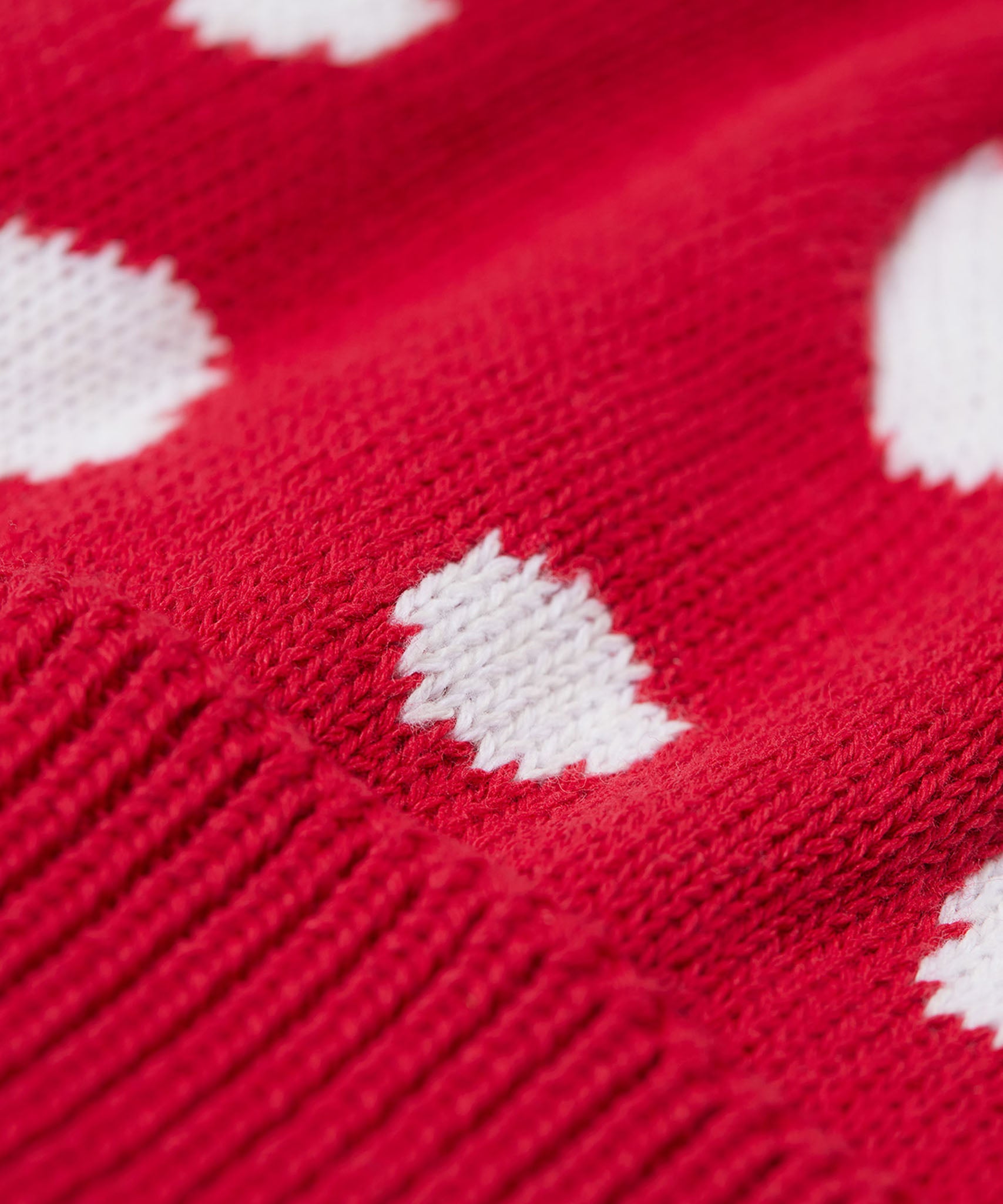 A close up of the Frugi kids noa knitted hat in red mushroom showing the red and white mushroom knit detail on organic cotton fabric