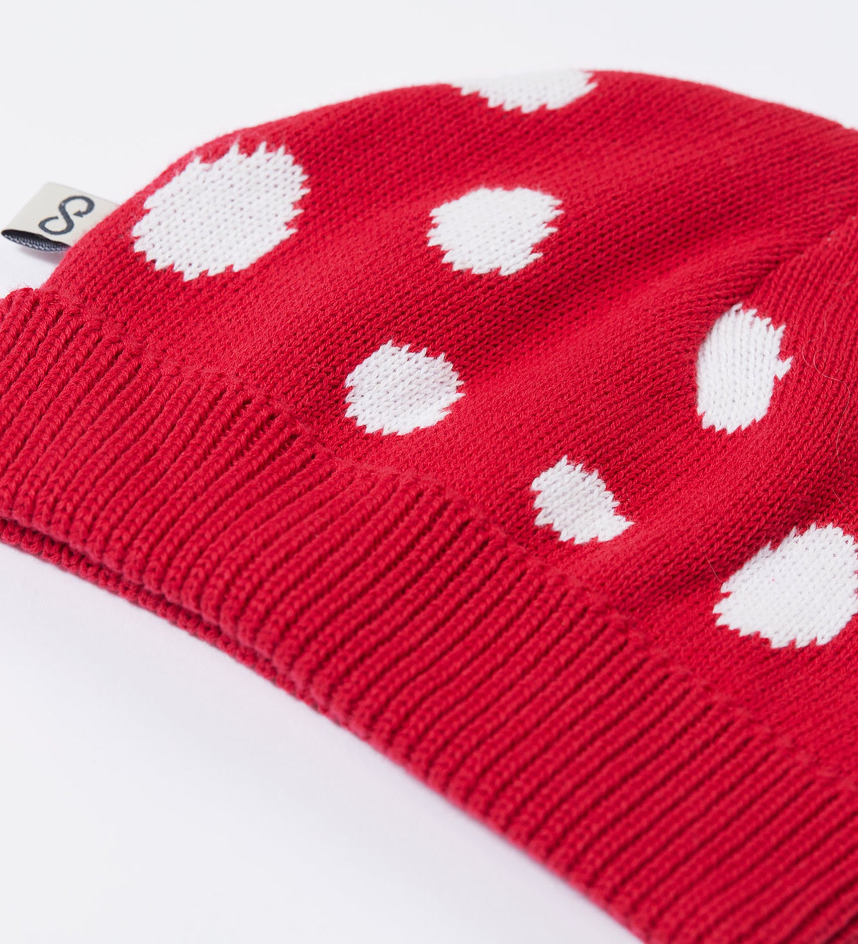 A close up of the Frugi kids noa knitted hat in red mushroom showing the ribbed brim detail on red organic cotton fabric