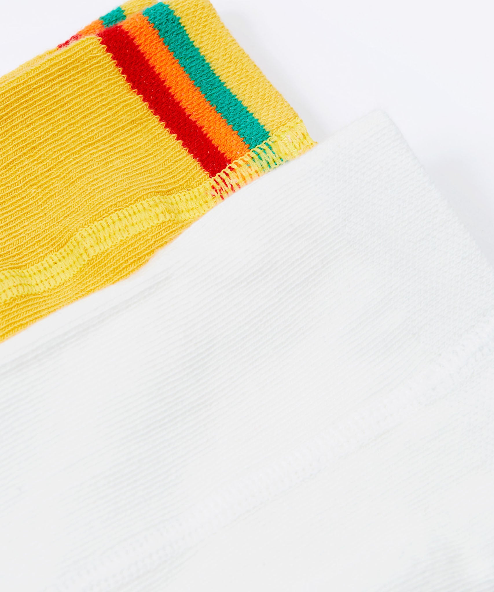 A close up of the waist bands on the Frugi Norah 2 pack tights. the flower design had a plain white waistband whilst the bumble bee yellow tights have a yellow, green, orange and red stripe on the waist band. 
