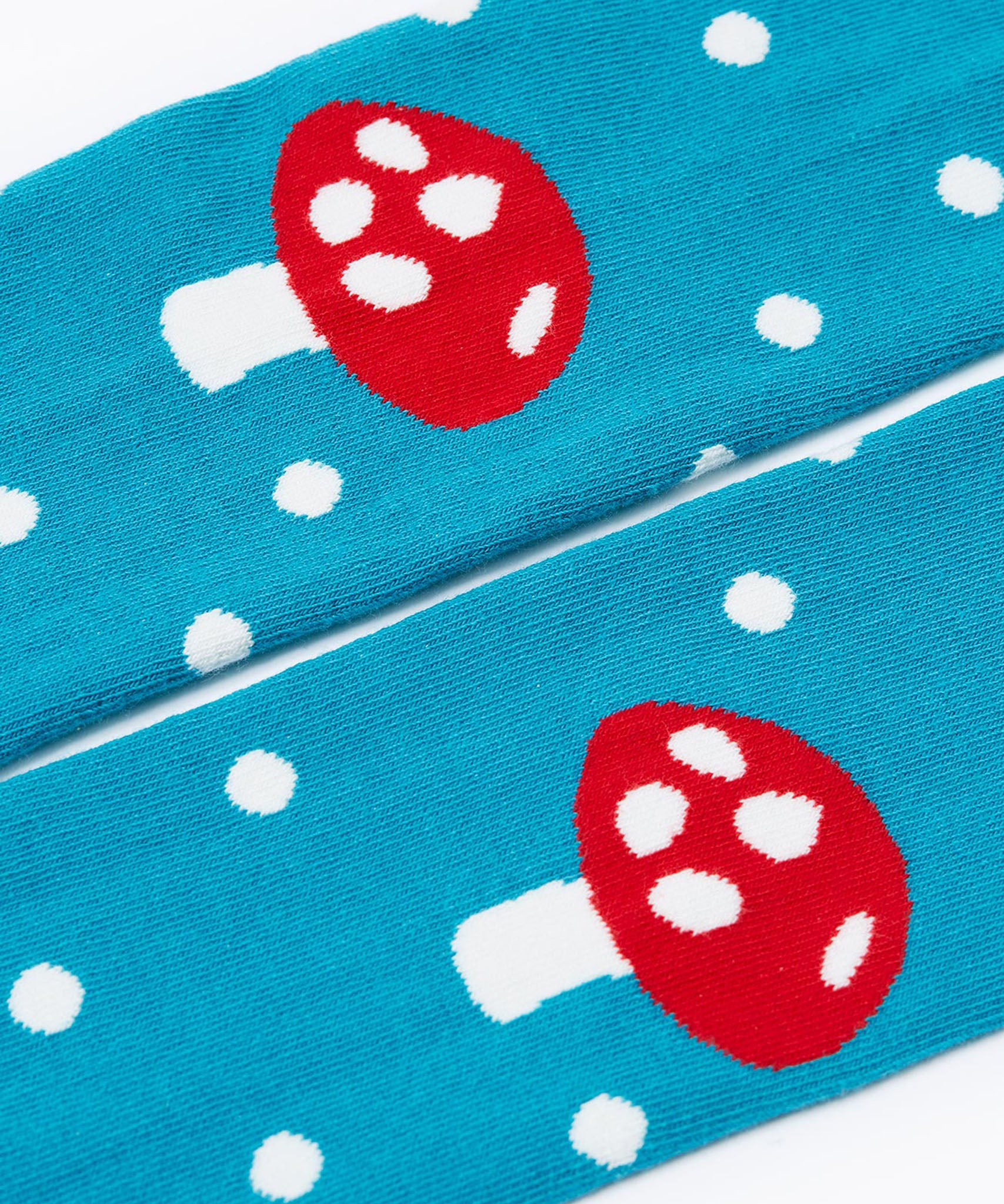 A close up of the knees on the mushroom design tights from the Frugi Norah 2 pack children's footed tights. The tights are turquoise blue with white spots all over the legs and the knees have a red mushroom on them.
