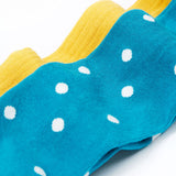 A close up of the blue coloured mushroom design tights from the Frugi Norah 2 pack tights. These child's footed tights have a turquoise blue background with white dots. The bumblebee yellow coloured tights can be seen in the background.