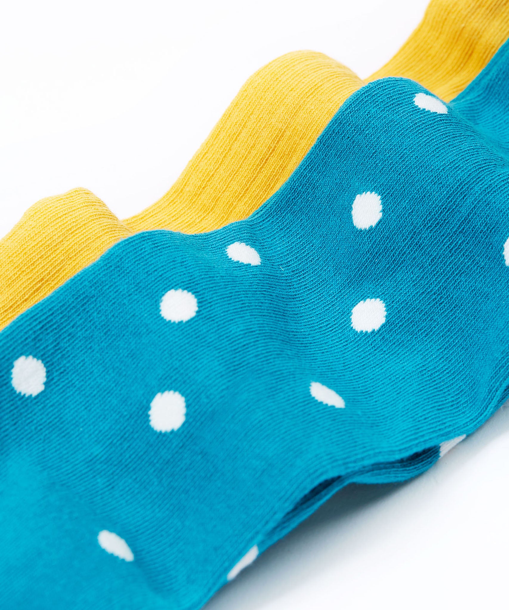 A close up of the blue coloured mushroom design tights from the Frugi Norah 2 pack tights. These child's footed tights have a turquoise blue background with white dots. The bumblebee yellow coloured tights can be seen in the background.