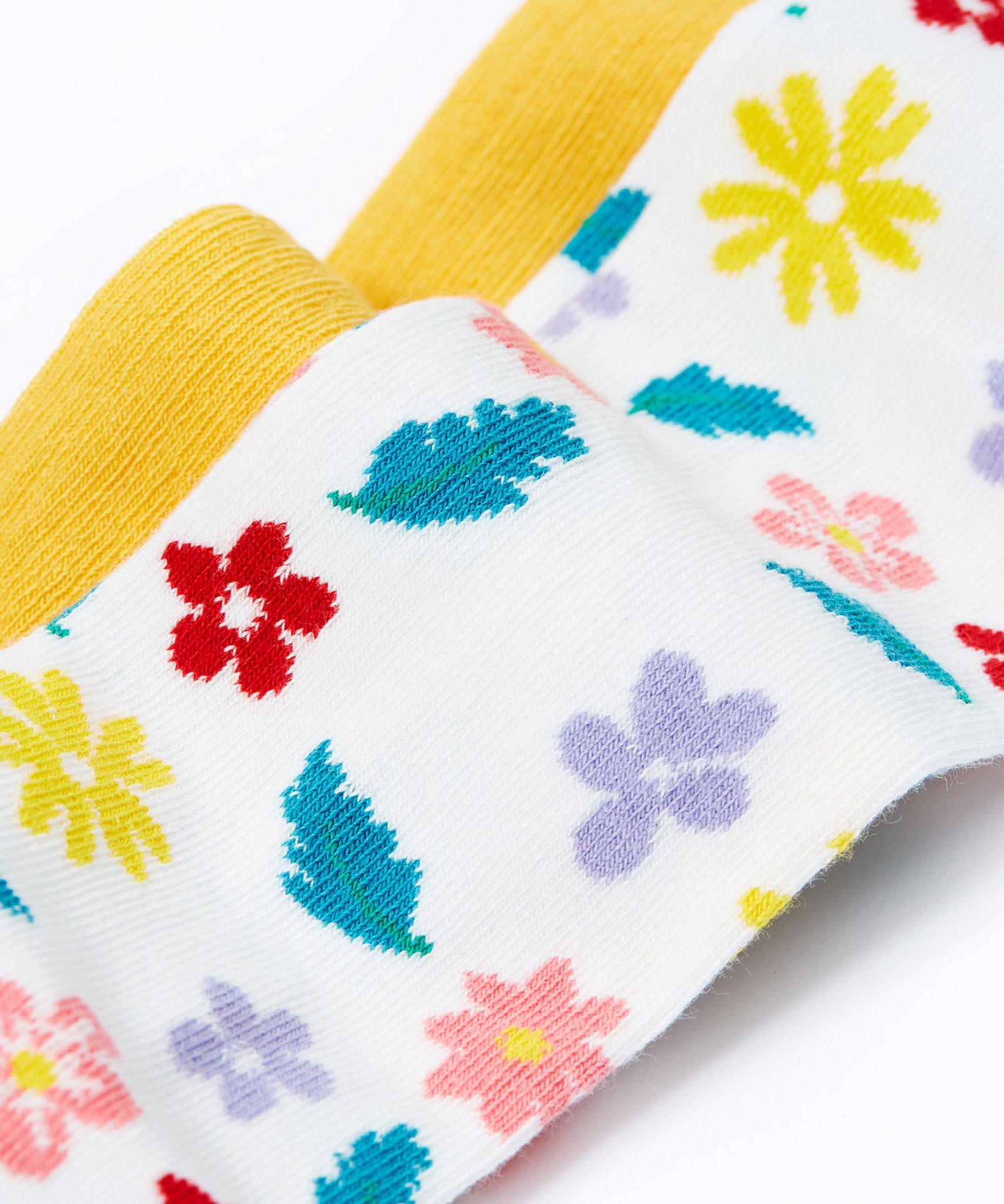 A close up of the print details on the Frugi flowers design tights from the Norah tights 2 pack. A white background with different coloured flowers and blue green coloured leaves all over the legs. 