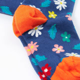 A close up of the feet on the Frugi Norah footed tights. A navy background with different coloured flowers and blue leaves all over the legs, the feet have solid orange coloured toe and heels.
