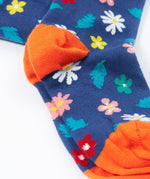 A close up of the feet on the Frugi Norah footed tights. A navy background with different coloured flowers and blue leaves all over the legs, the feet have solid orange coloured toe and heels.