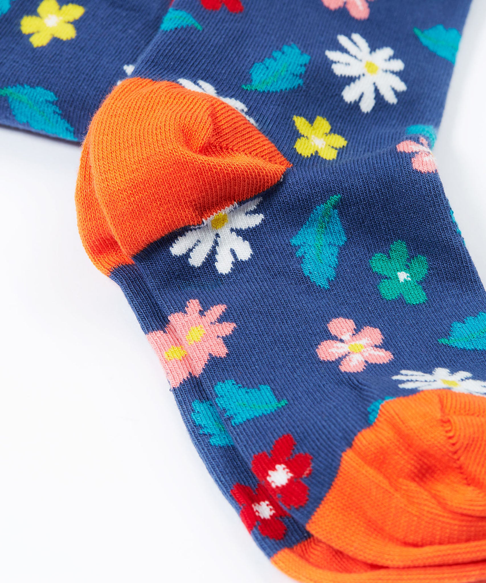 A close up of the feet on the Frugi Norah footed tights. A navy background with different coloured flowers and blue leaves all over the legs, the feet have solid orange coloured toe and heels.
