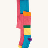 A 2 pack of Frugi Norah organic cotton footed kids tights. One pair has a multi-colour hotchpotch colour block design the other has a solid rose pink colour with multi-coloured waistband. 