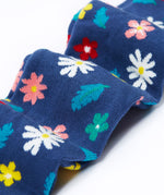 A close up of the legs on the Frugi Norah footed navy flowers tights. The flowers design features  different coloured flowers and blue leaves all print on a navy background.
