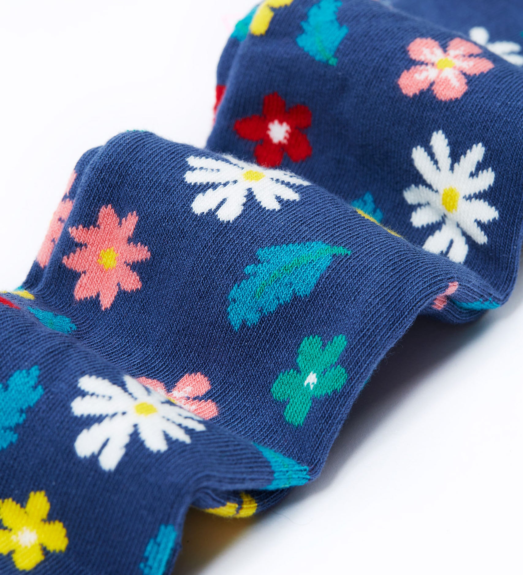 A close up of the legs on the Frugi Norah footed navy flowers tights. The flowers design features  different coloured flowers and blue leaves all print on a navy background.
