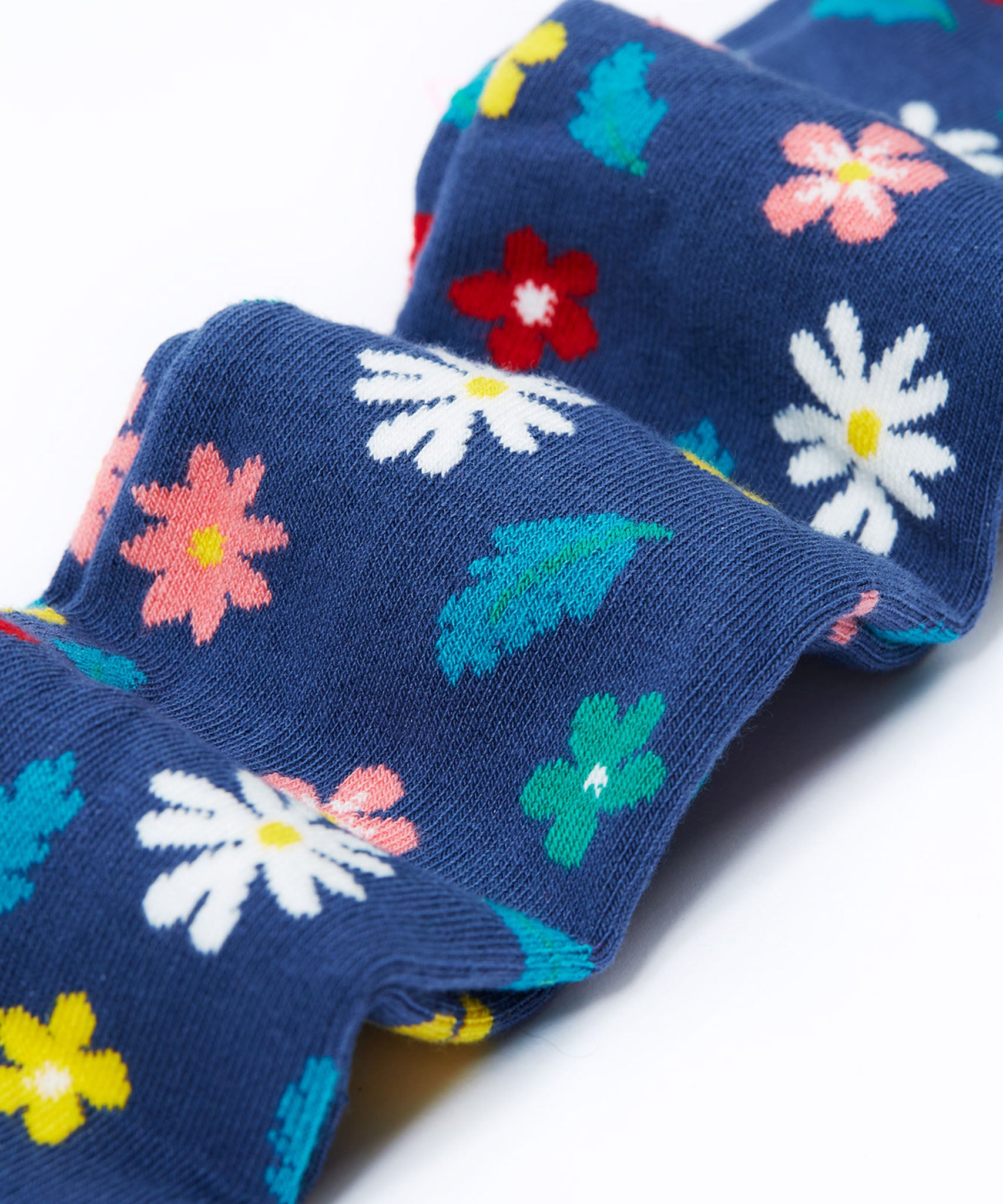 A close up of the legs on the Frugi Norah footed navy flowers tights. The flowers design features  different coloured flowers and blue leaves all print on a navy background.
