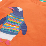 Close up of the Frugi organic cotton superb sweatshirt salamander orange with penguin applique. The penguin is wearing a fairisle style tank top. 