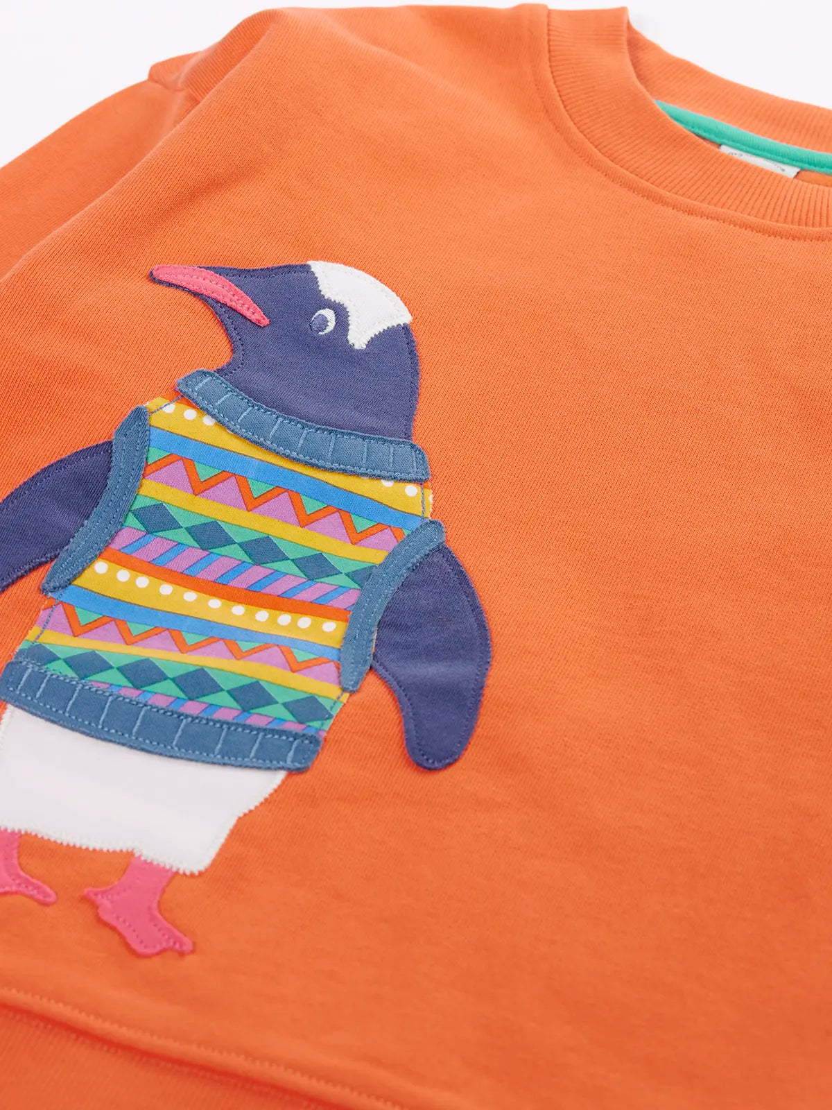 Close up of the Frugi organic cotton superb sweatshirt salamander orange with penguin applique. The penguin is wearing a fairisle style tank top. 