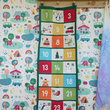 Colourful Frugi forest festive fun organic cotton advent calendar hung up on wooden peg in the Babipur playroom. 24 pockets with alternating colourful illustrations and colour blocks. 