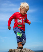 Child wearing the Frugi red organic cotton adventure magic applique top. Long sleeved top with castle, rainbow, tree horse and nessie appliques on the front. 