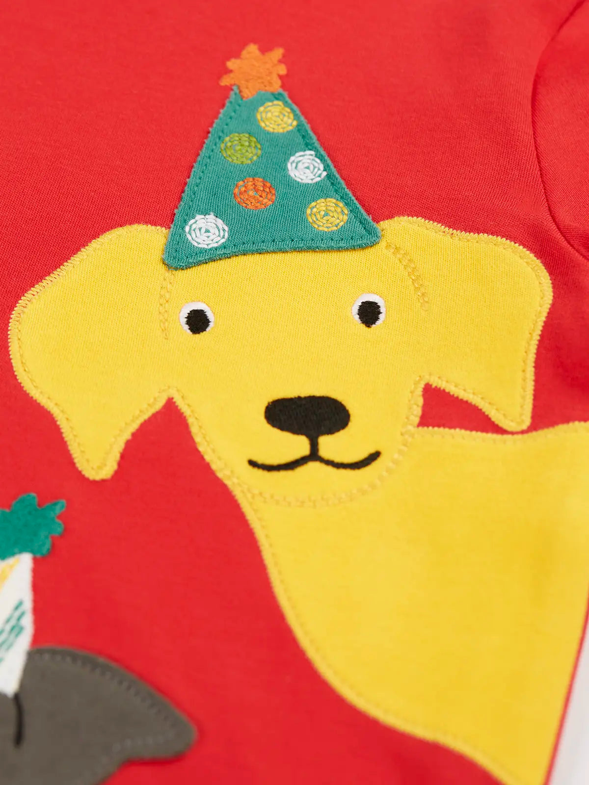 Close up of the yellow Labrador dog wearing a green party hat applique on the Frugi organic cotton adventure circular long sleeve top .