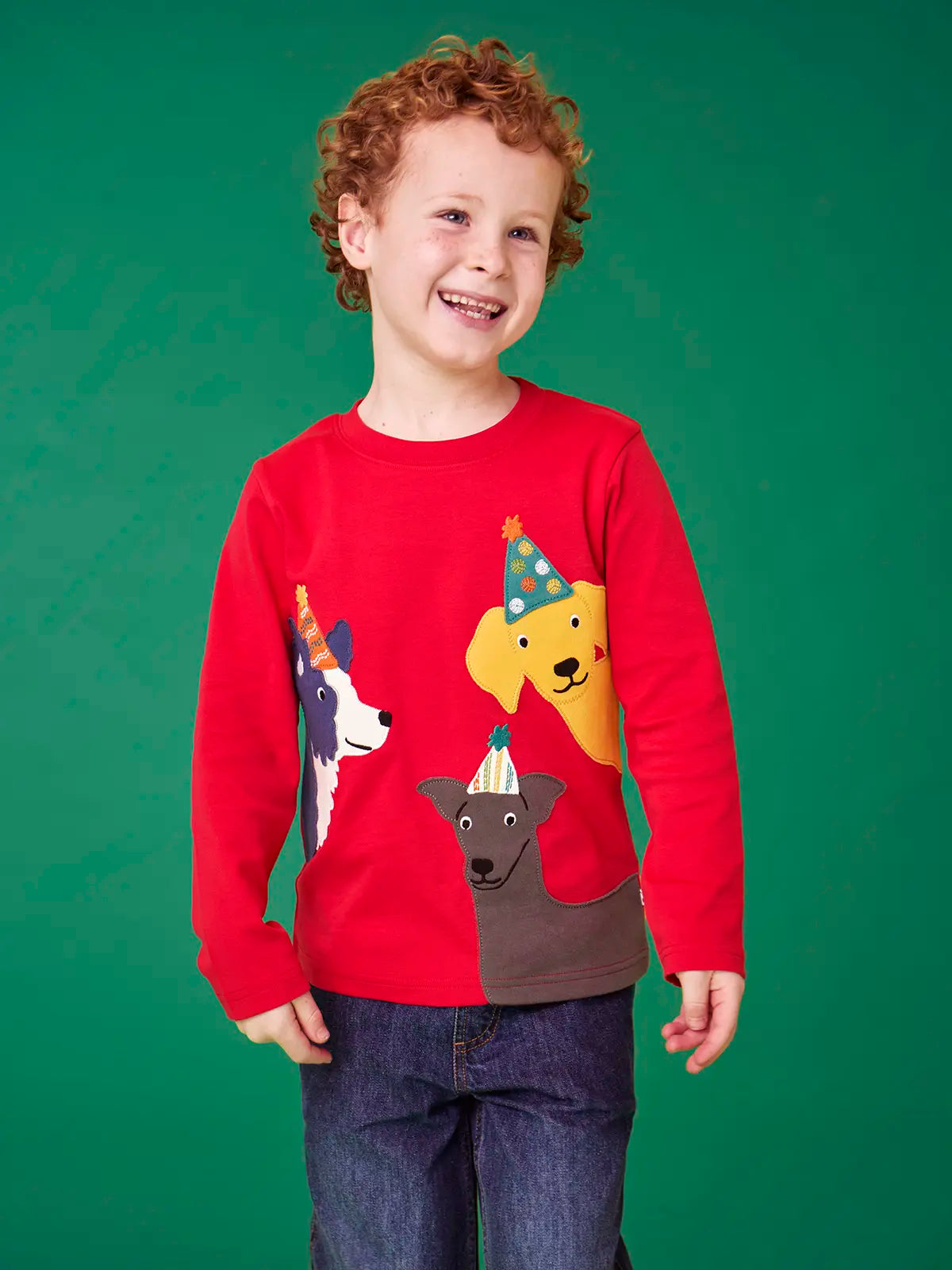 Child wearing the Frugi organic cotton adventure circular long sleeve top scarlet red with three dogs wearing party hats on the front. 